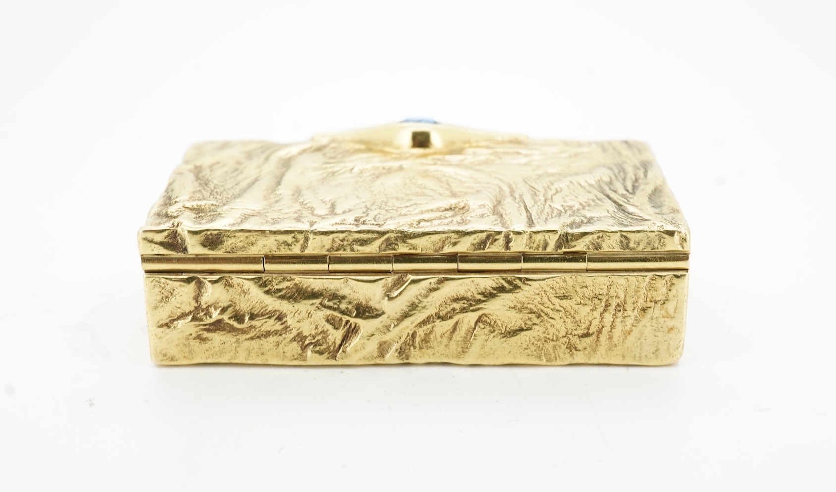 Dunhill, an attractive 9ct gold and sapphire snuffbox, circa 1973, the rectangular box of samorodok finish, the hinged lid set with a foil-backed oval sapphire, measuring approximately 5.1 x 2.7 x 1.6cm, signed Dunhill L